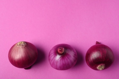 Photo of Whole red onion bulbs on pink background, flat lay. Space for text