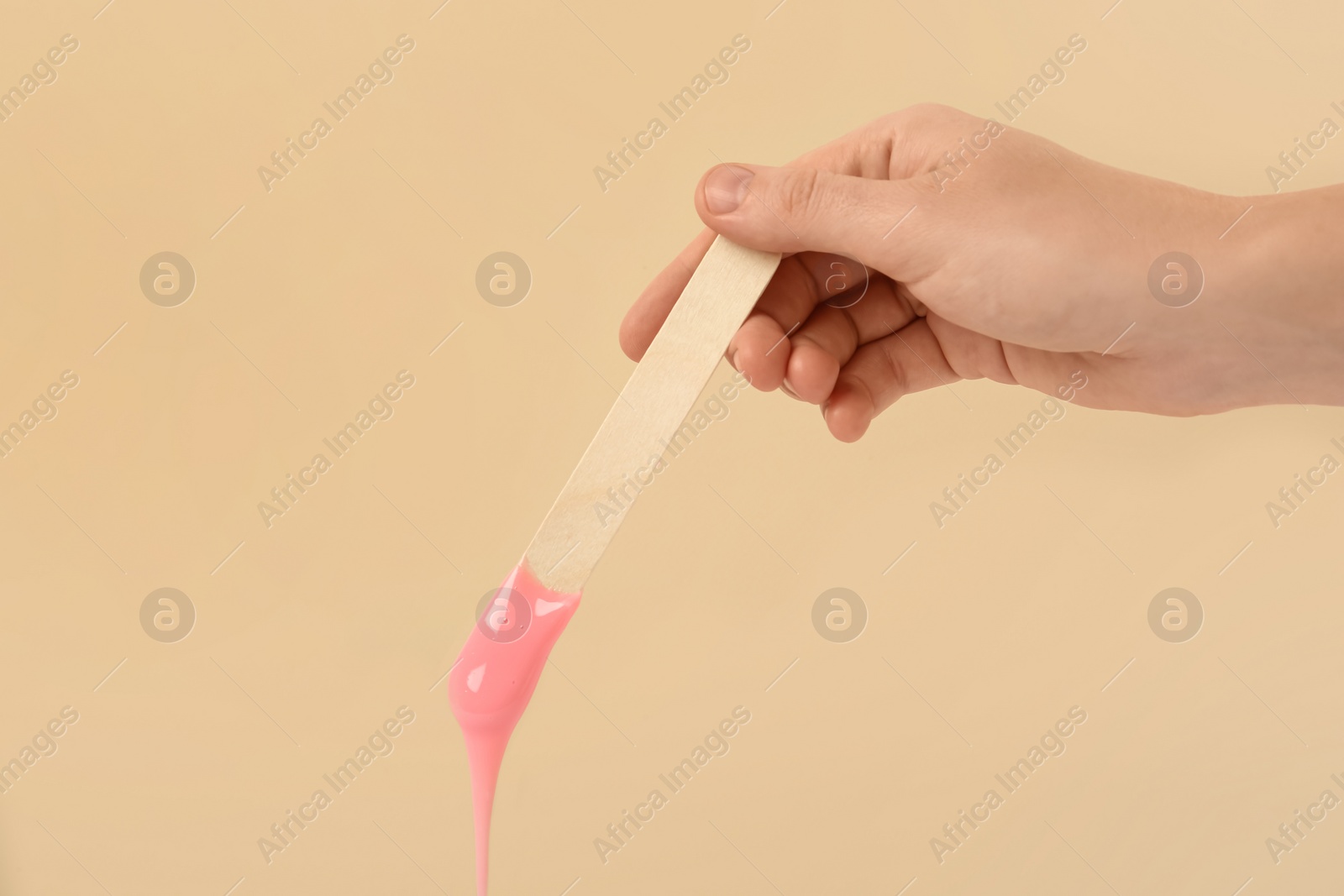 Photo of Woman holding spatula with hot depilatory wax on beige background, closeup