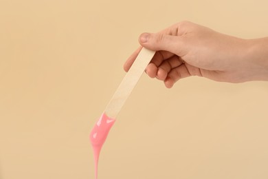 Woman holding spatula with hot depilatory wax on beige background, closeup