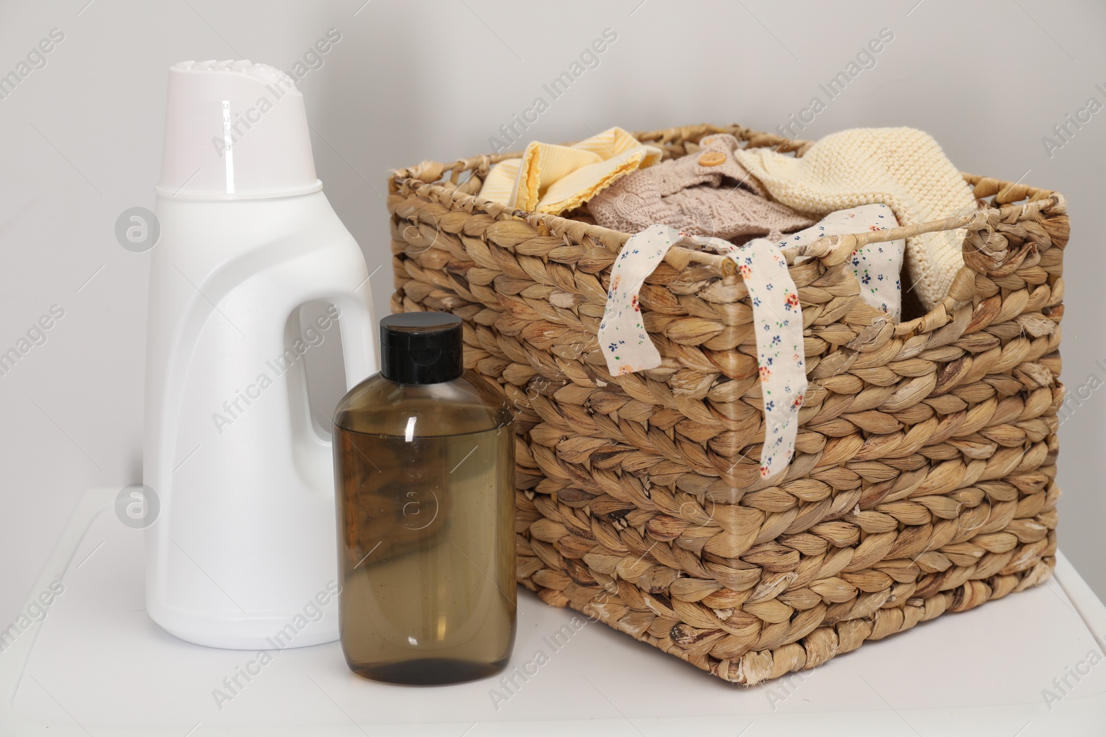 Photo of Baby clothes in wicker basket and laundry detergents on washing machine near light wall