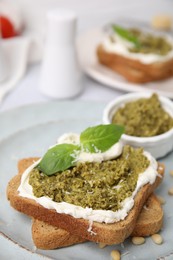 Tasty bruschetta with cream cheese, pesto sauce and fresh basil on plate, closeup