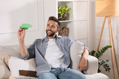 Photo of Handsome man playing with paper plane in living room at home