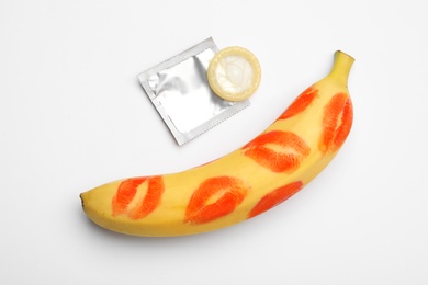 Photo of Condom and banana with lipstick kiss marks on white background, top view. Safe sex