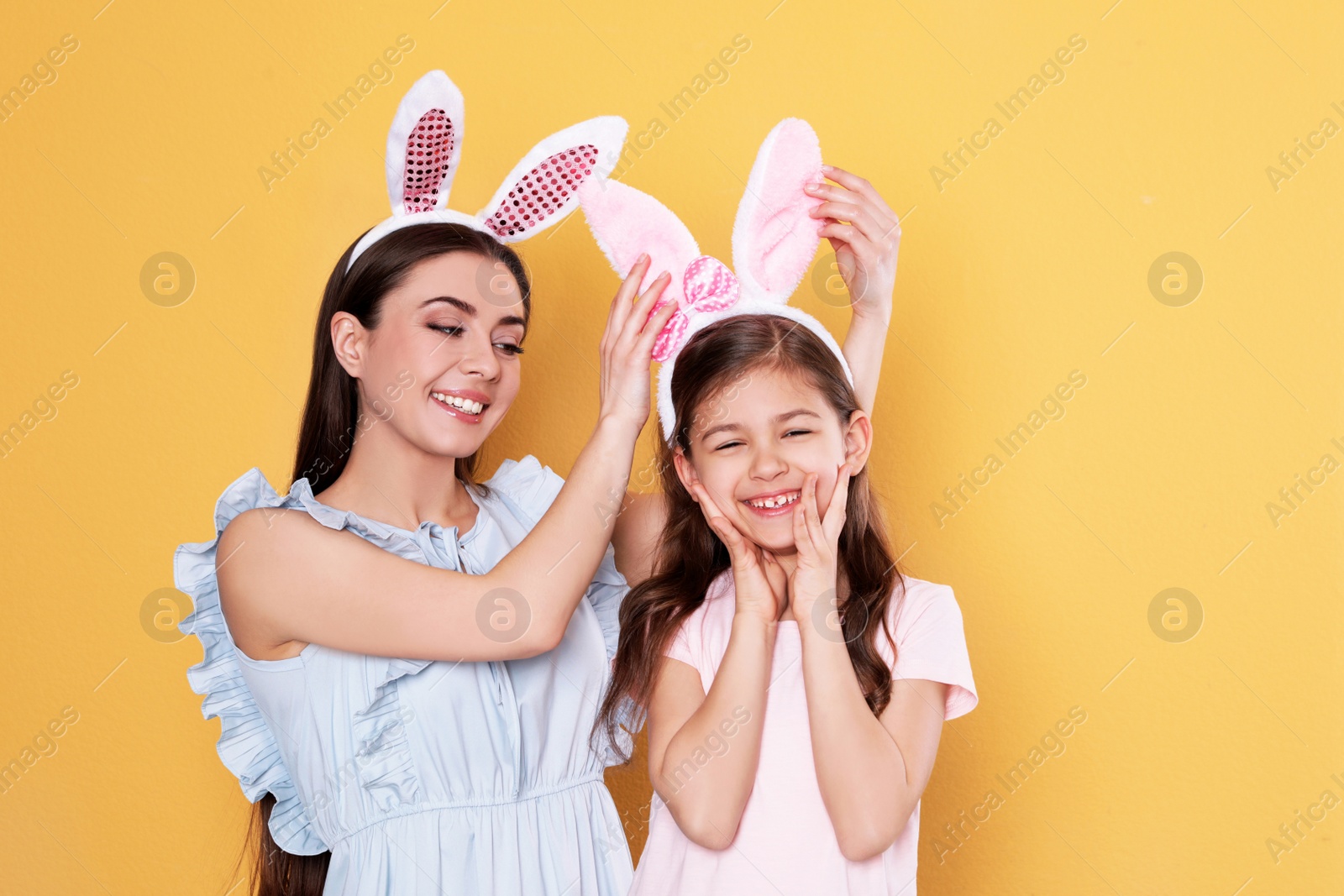 Photo of Mother and daughter in Easter bunny ears headbands on color background