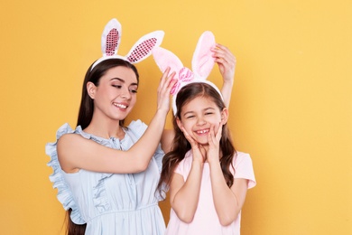 Photo of Mother and daughter in Easter bunny ears headbands on color background