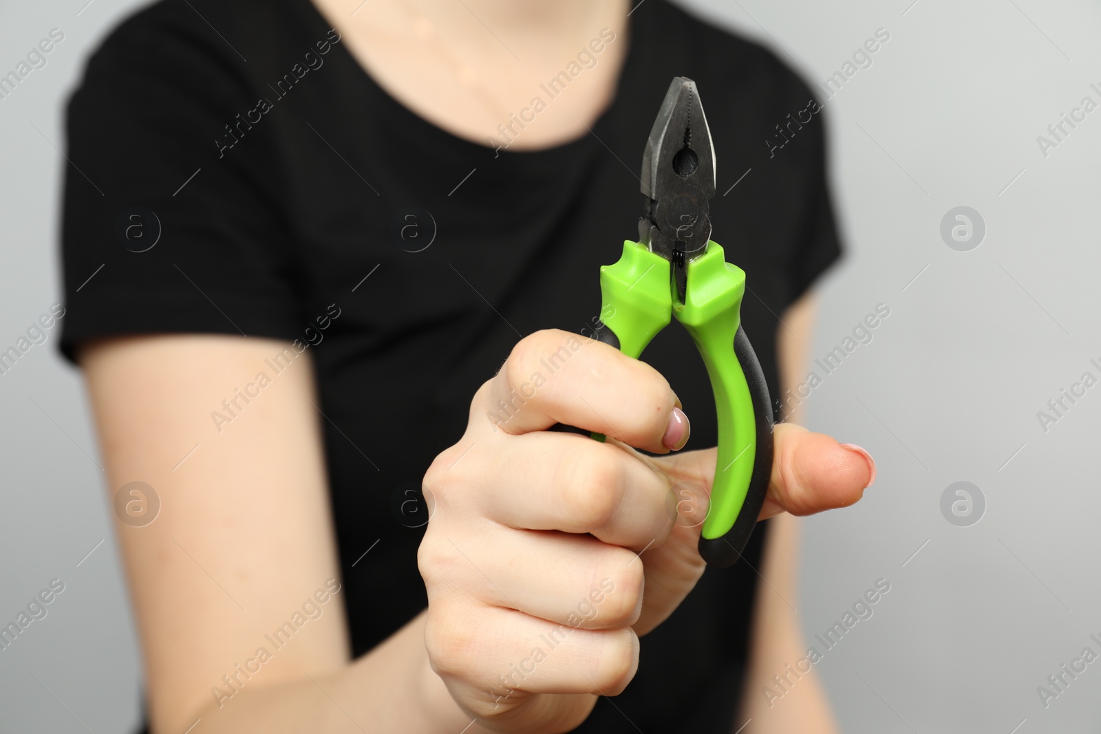 Photo of Woman with combination pliers on grey background, closeup