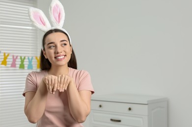 Happy woman wearing bunny ears headband in decorated room, space for text. Easter celebration
