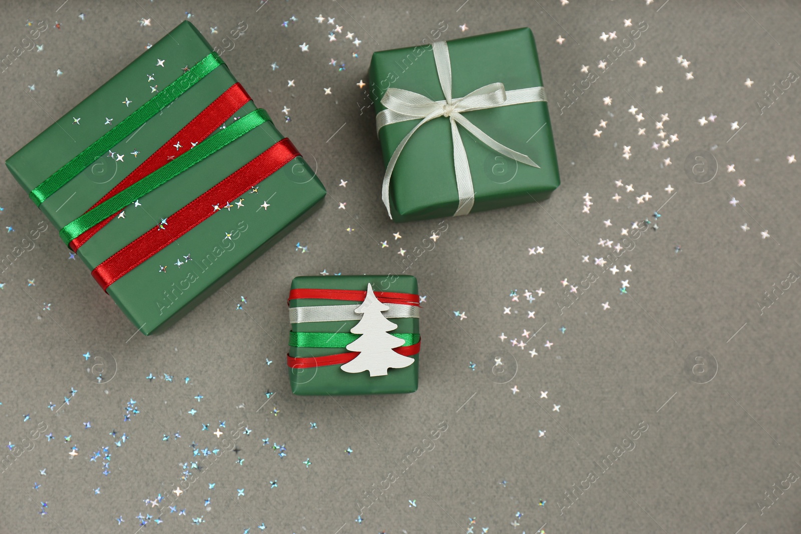 Photo of Christmas gift boxes and shiny confetti on grey background, flat lay. Space for text