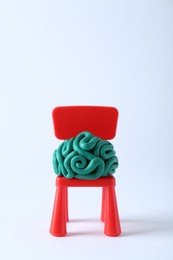 Brain made of plasticine on mini chair against white background