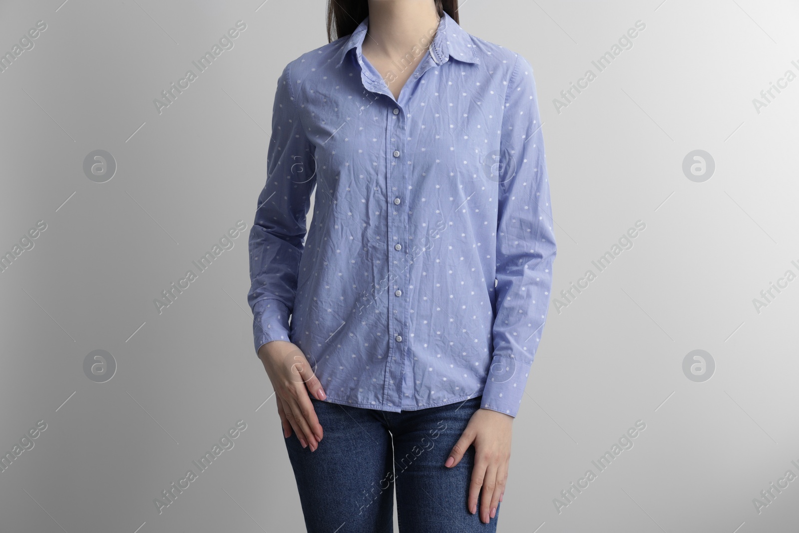 Photo of Woman wearing wrinkled light blue polka dot blouse on light grey background, closeup