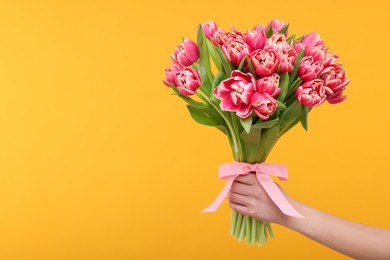 Woman holding beautiful bouquet on orange background, closeup. Space for text