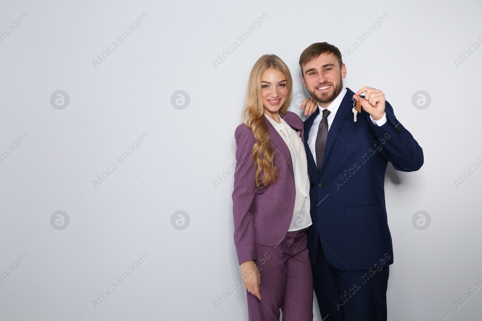 Photo of Happy young business people with house key on light background, space for text