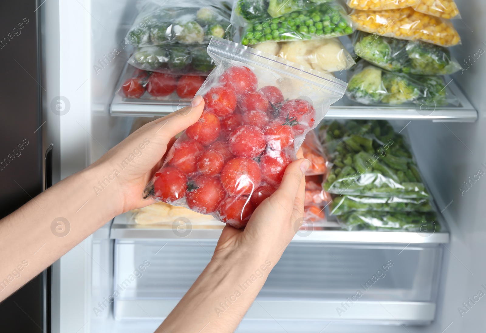 Photo of Woman holding plastic bag with frozen tomatoes near open refrigerator, closeup