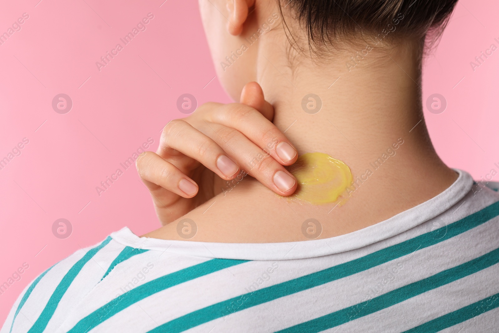 Photo of Woman applying ointment onto her neck on pink background, closeup