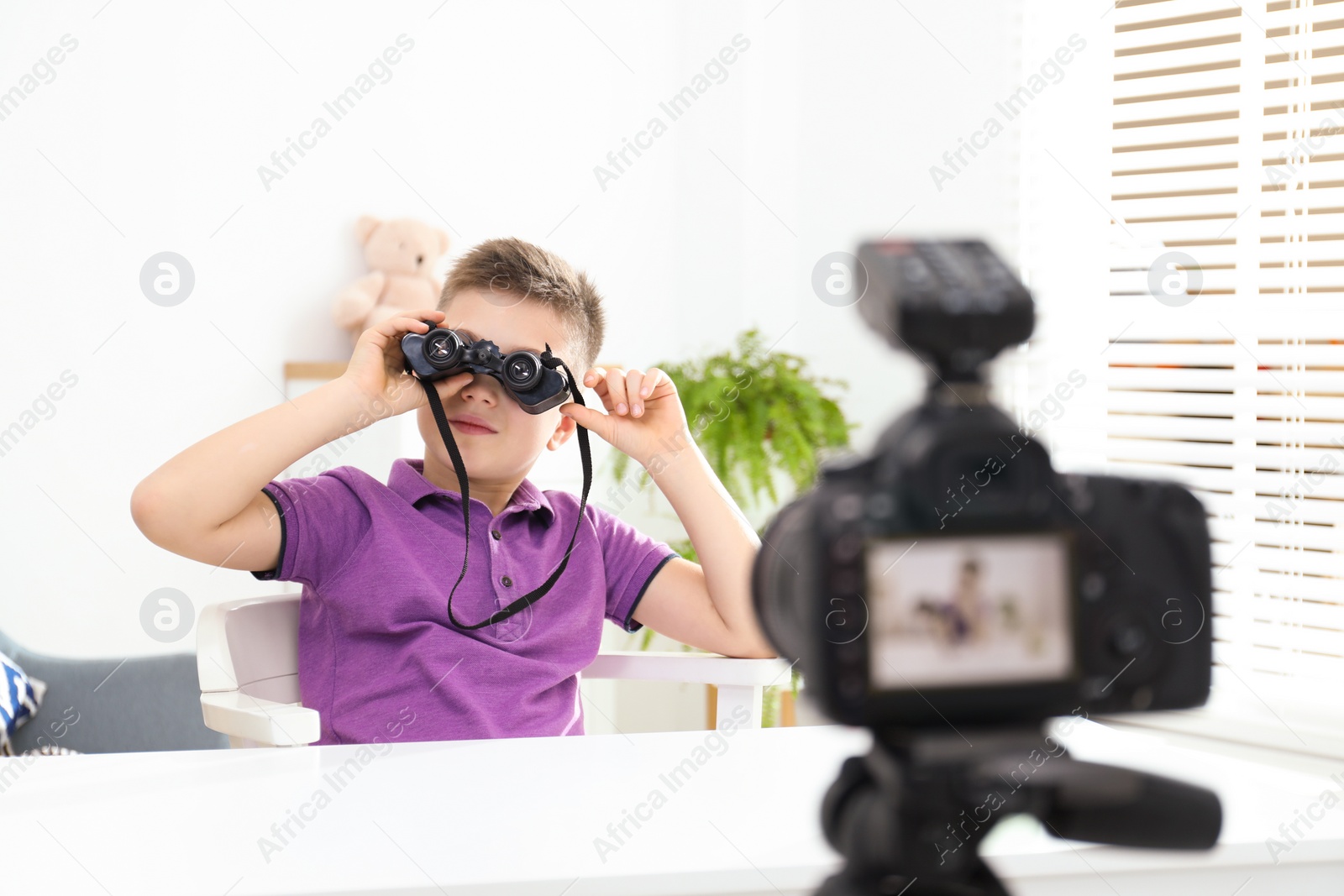 Photo of Cute little blogger with binoculars recording video at home