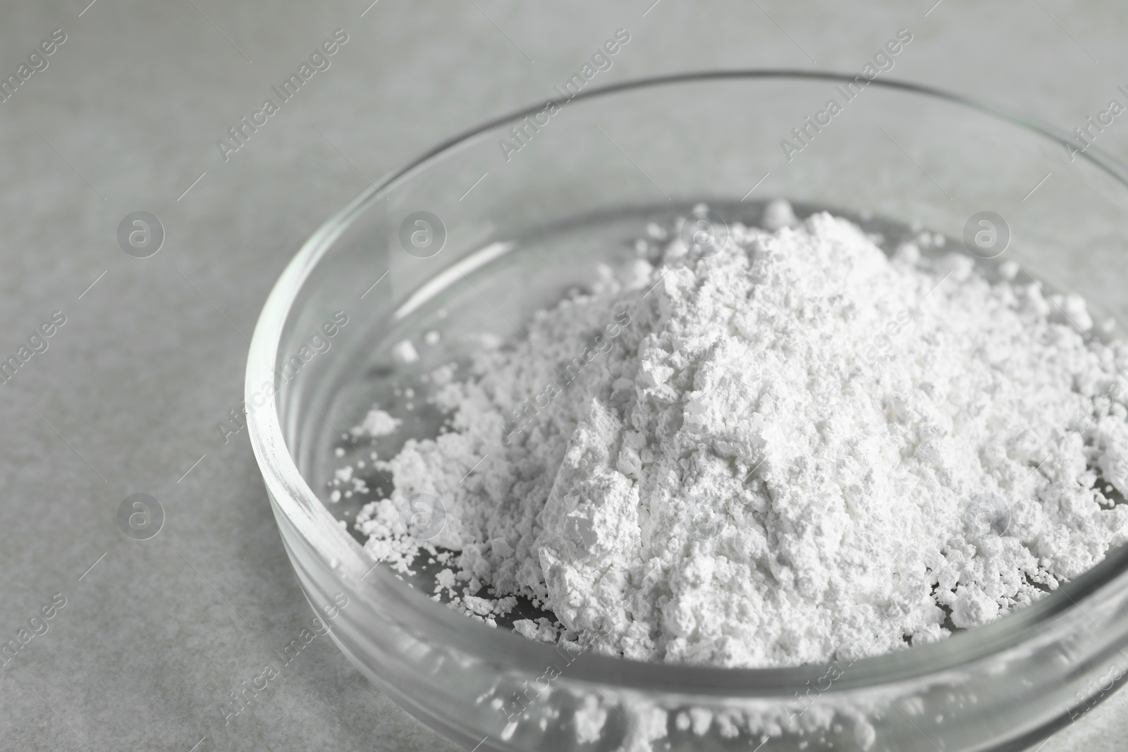 Photo of Petri dish with calcium carbonate powder on light grey table, closeup