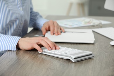 Professional accountant using calculator at wooden desk in office, closeup