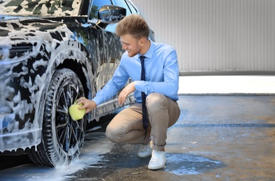 Businessman cleaning auto with sponge at self-service car wash