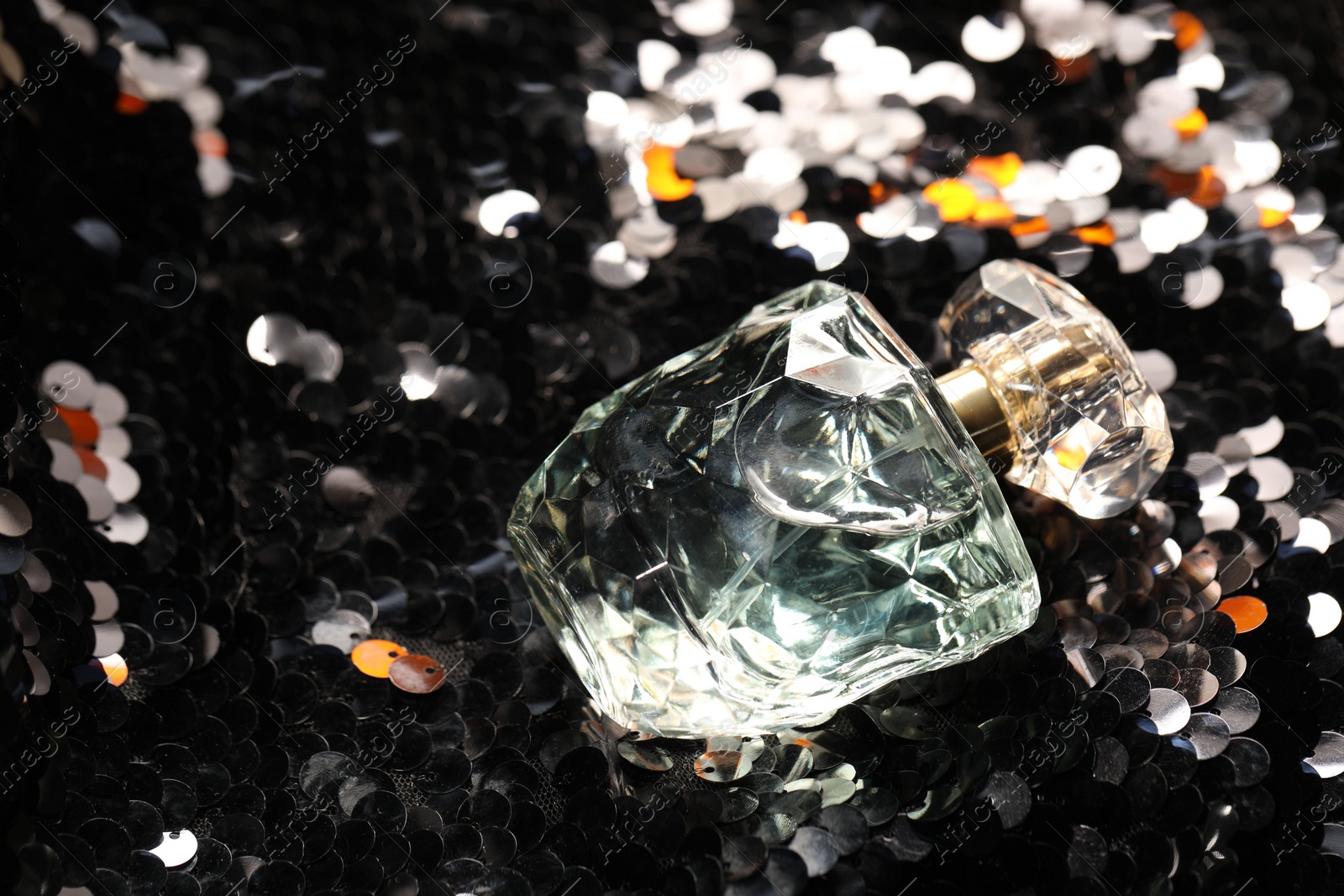 Photo of Luxury perfume in bottle on fabric with shiny sequins, closeup