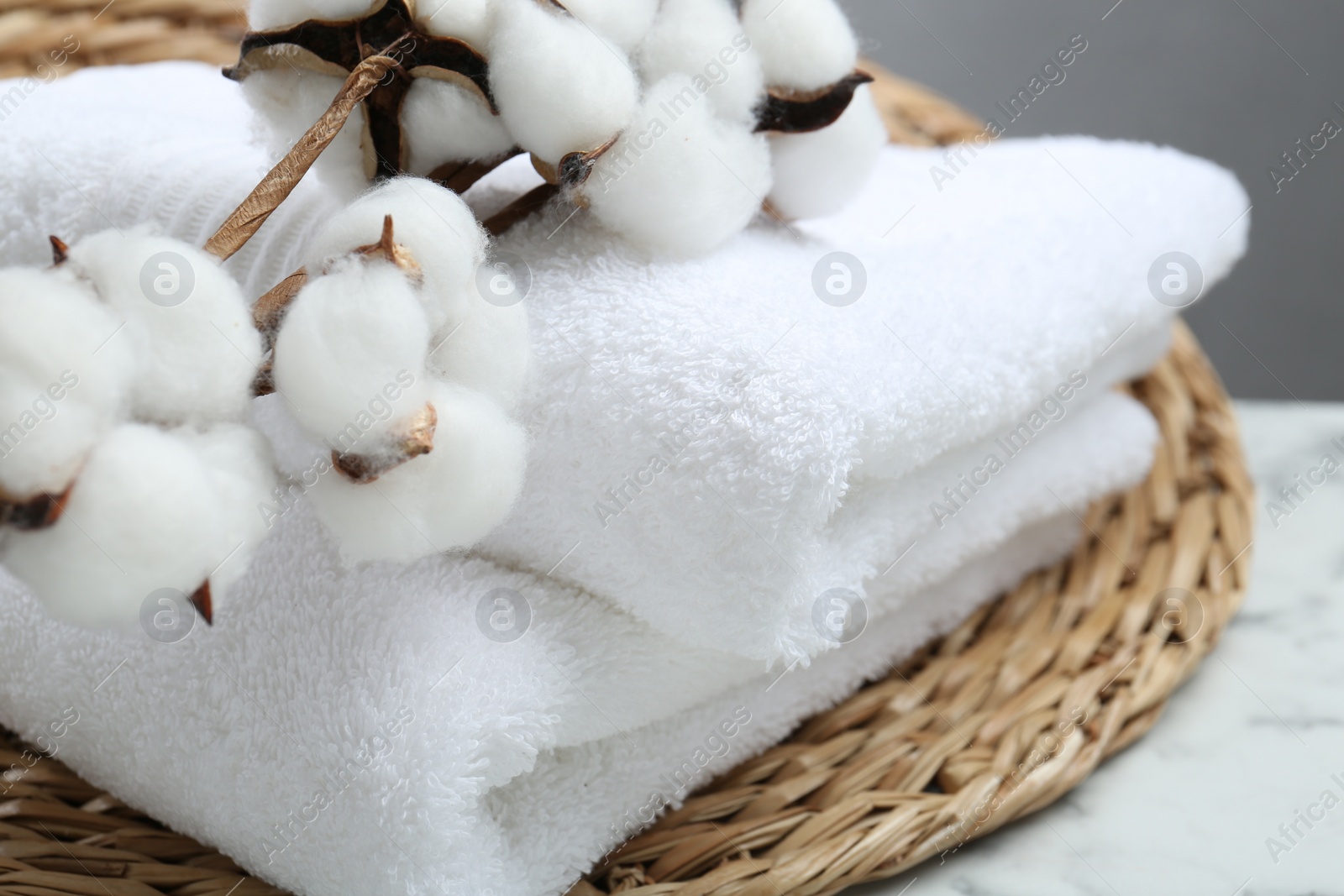 Photo of Folded terry towels and cotton flowers on white table, closeup