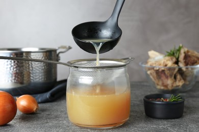 Photo of Sieving delicious bone broth into glass jar on grey table