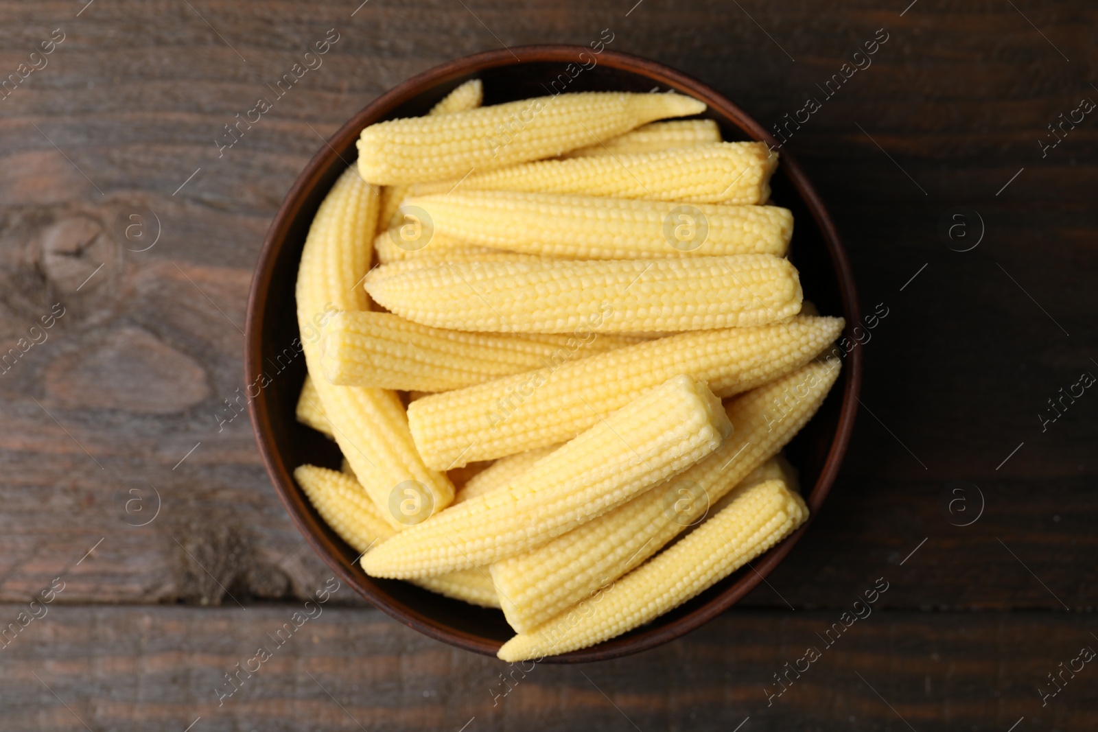 Photo of Tasty fresh yellow baby corns in bowl on wooden table, top view