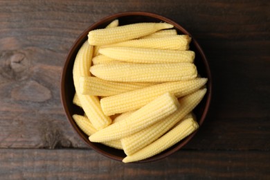 Tasty fresh yellow baby corns in bowl on wooden table, top view