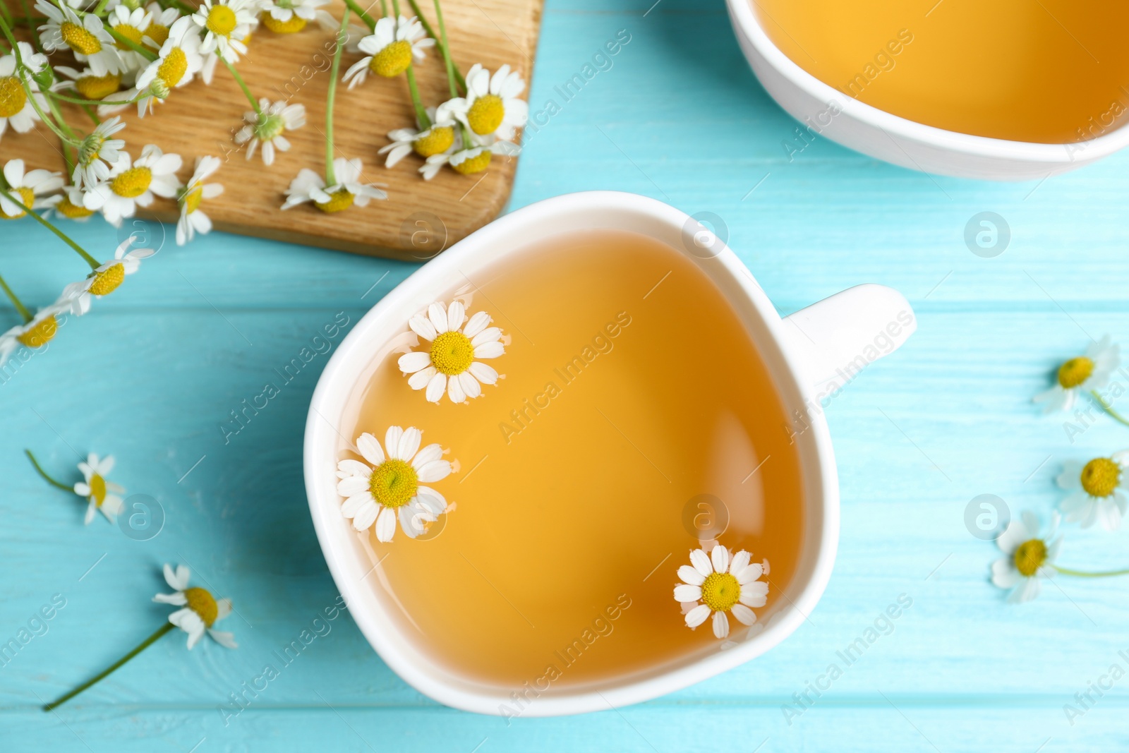 Photo of Fresh chamomile tea in cup on light blue wooden table, flat lay