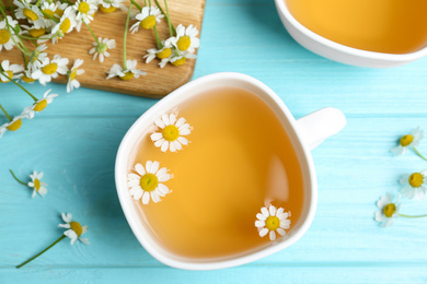 Photo of Fresh chamomile tea in cup on light blue wooden table, flat lay