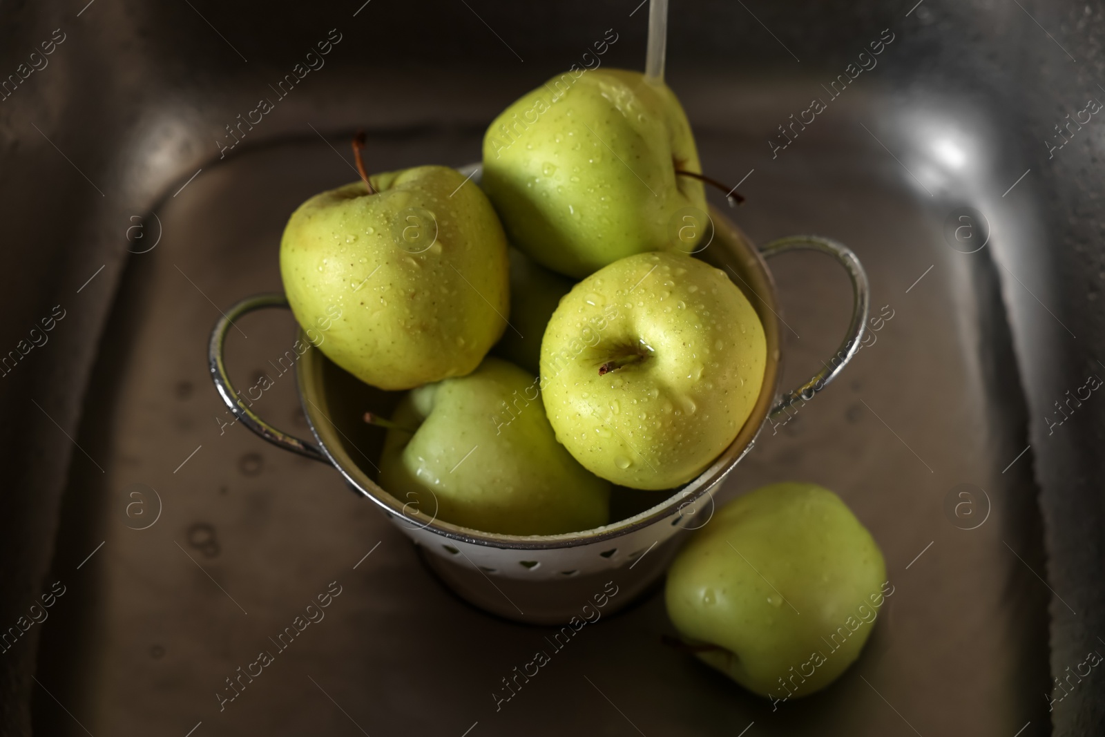 Photo of Washing fresh apples with tap water in metal colander inside sink