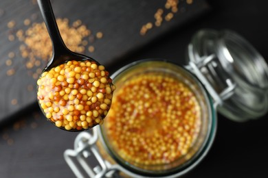 Photo of Spoon with whole grain mustard over jar on table, closeup