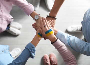 Image of Help for Ukraine. People holding hands together with drawings of Ukrainian flag, top view