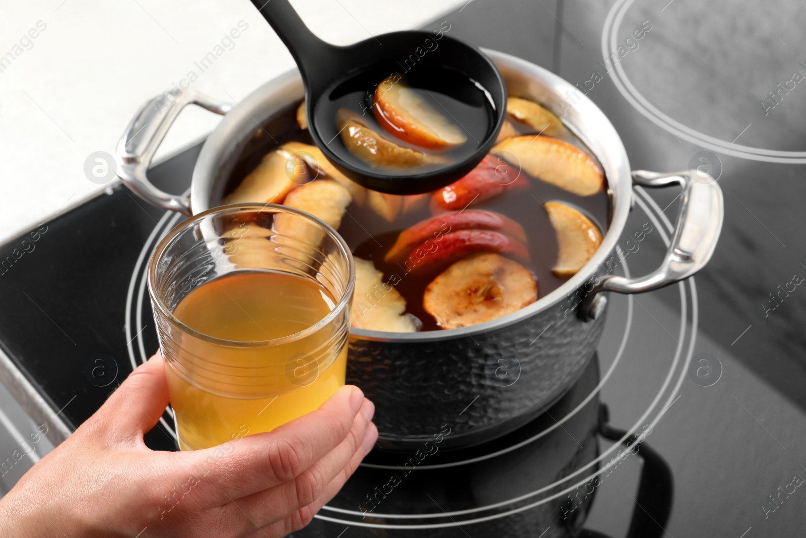 Photo of Woman pouring compot into glass near stove, closeup