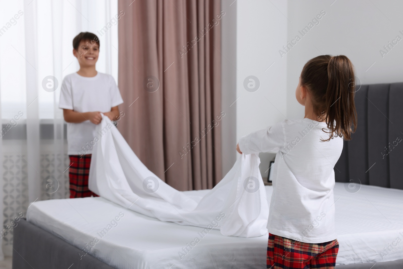 Photo of Brother and sister changing bed linens together in bedroom