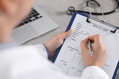 Doctor filling out patient's medical card at table in clinic, closeup