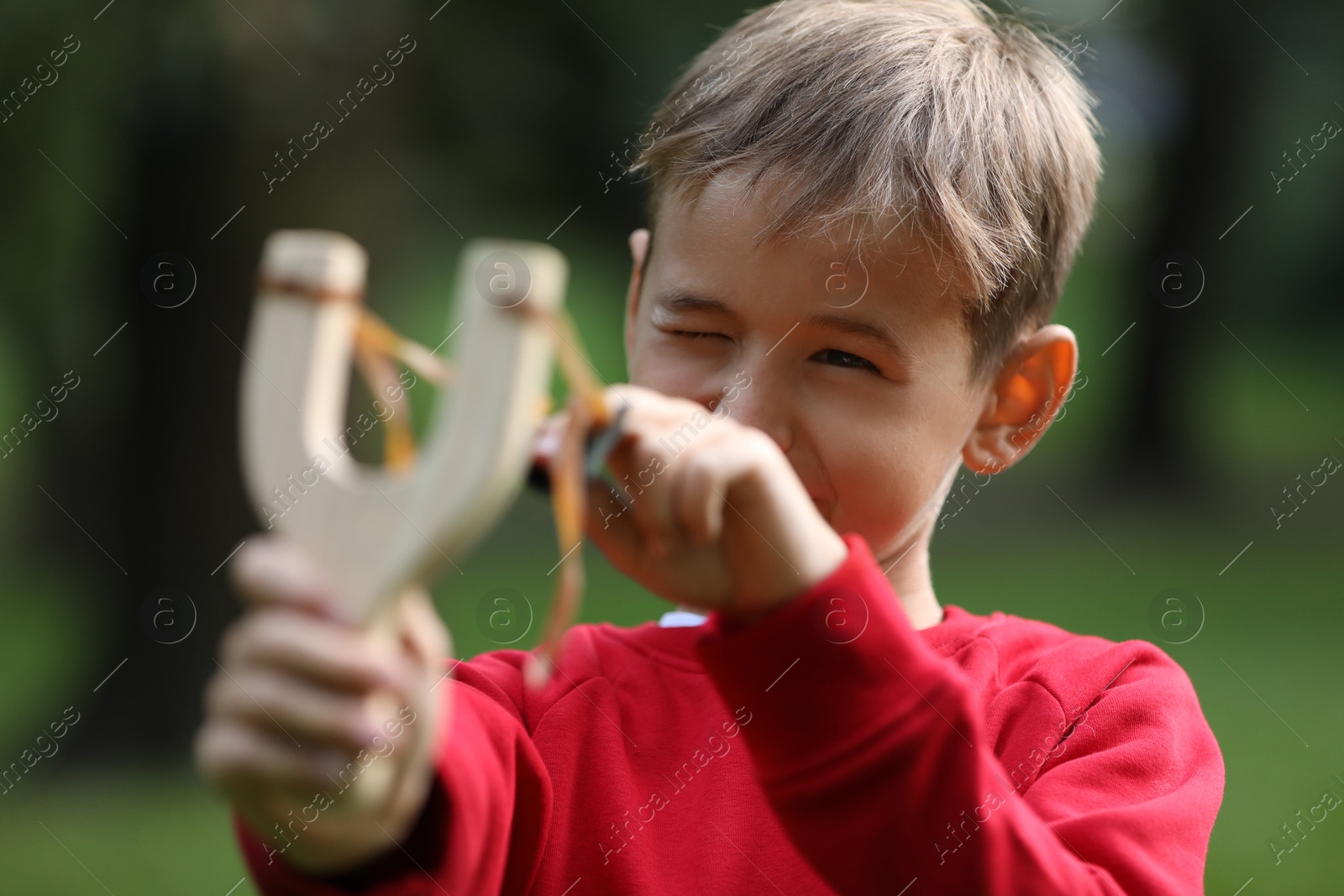 Photo of Little boy playing with slingshot in park