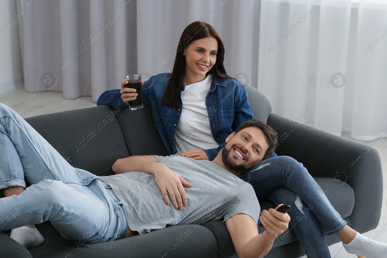 Photo of Happy couple watching show at home. Man changing TV channels with remote control