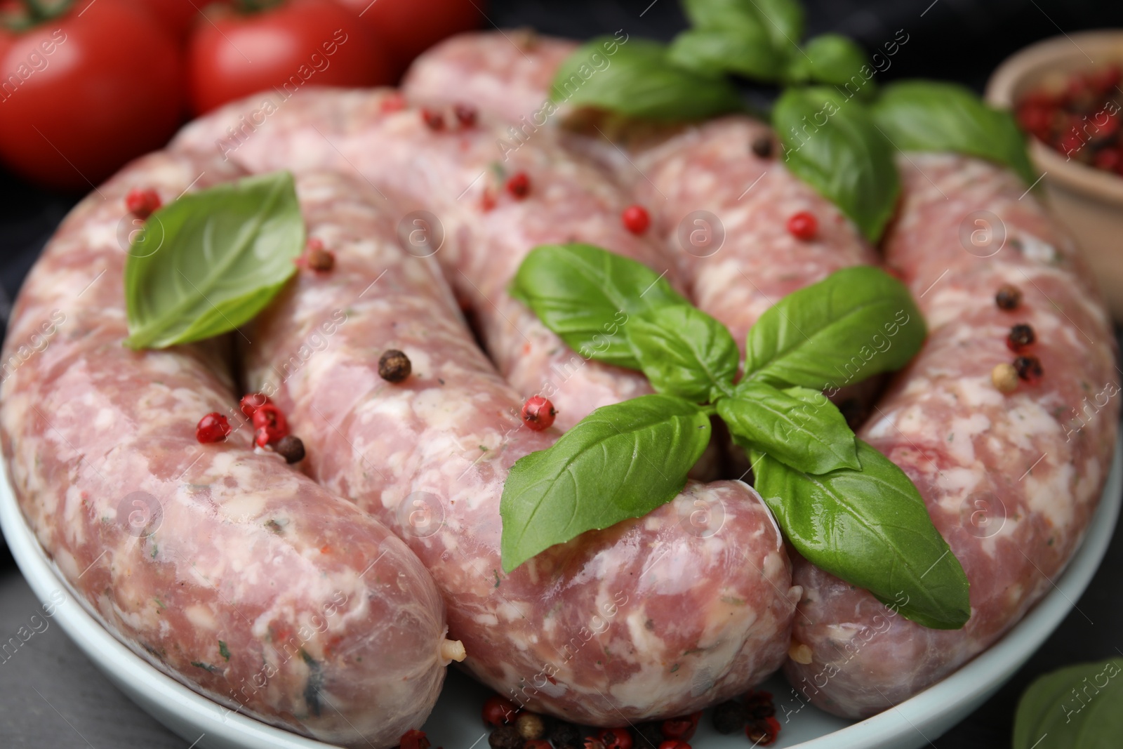 Photo of Raw homemade sausages, basil leaves and peppercorns on table, closeup