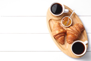 Photo of Tasty breakfast. Cups of coffee, jam and croissants on white wooden table, top view. Space for text