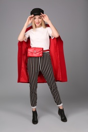 Photo of Young stylish woman in trendy shoes with bum bag on grey background