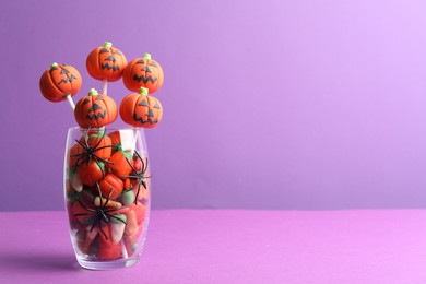 Photo of Delicious pumpkin shaped cake pops on violet background, space for text. Halloween treat