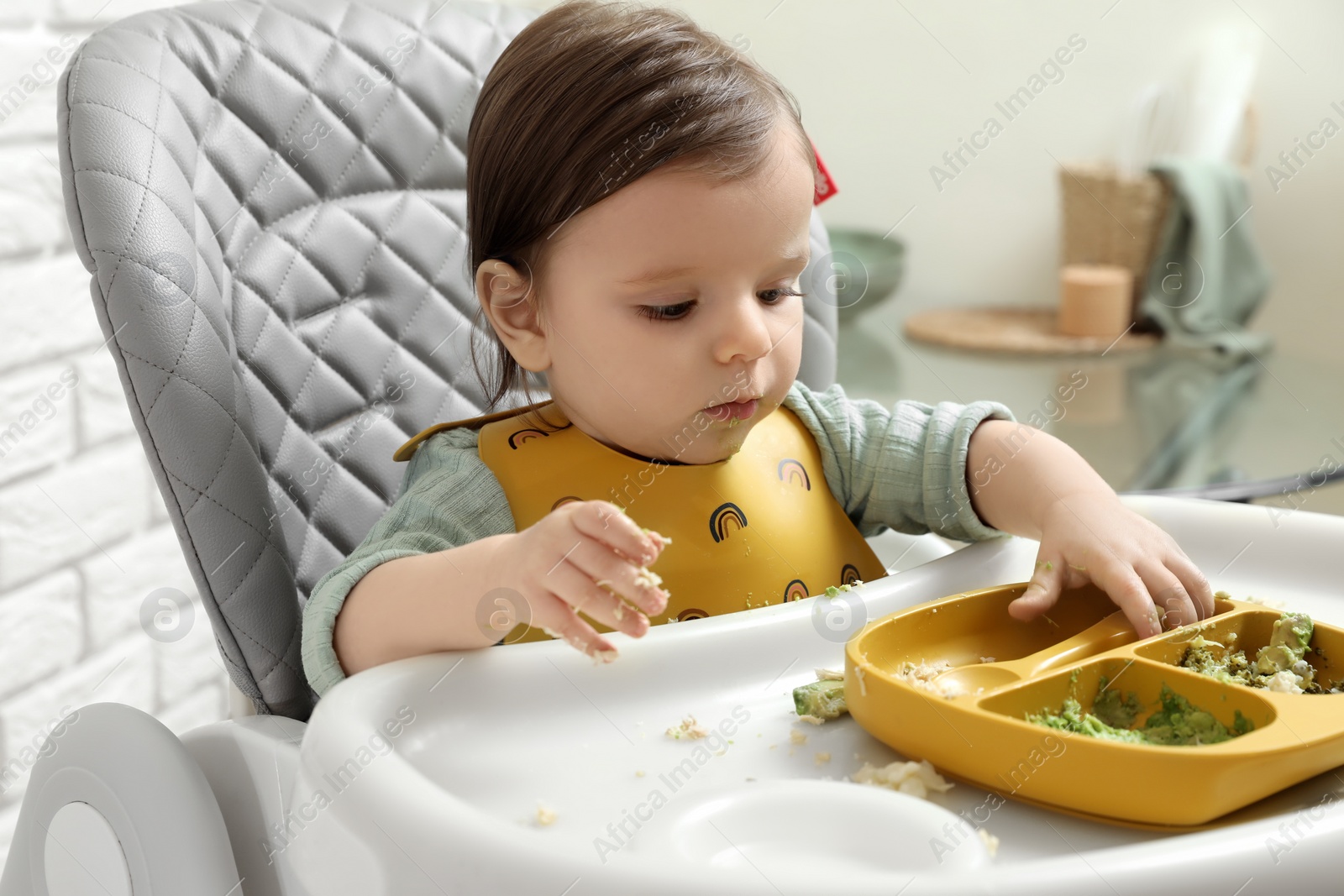 Photo of Cute little baby eating healthy food in high chair indoors