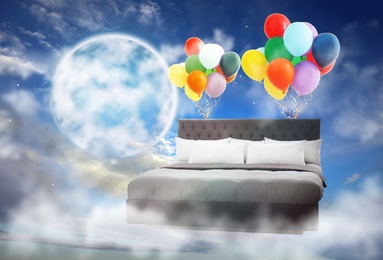 Sweet dreams. Bed with bright air balloons near full moon in cloudy sky