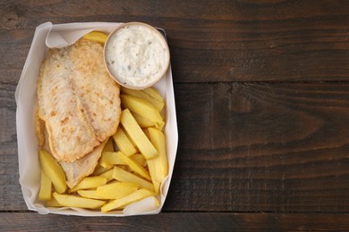 Photo of Delicious fish and chips with tasty sauce in paper box on wooden table, top view. Space for text