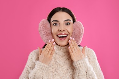 Photo of Beautiful young woman wearing earmuffs on pink background