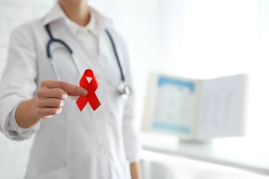 Doctor holding red ribbon on blurred background, closeup with space for text. AIDS awareness month