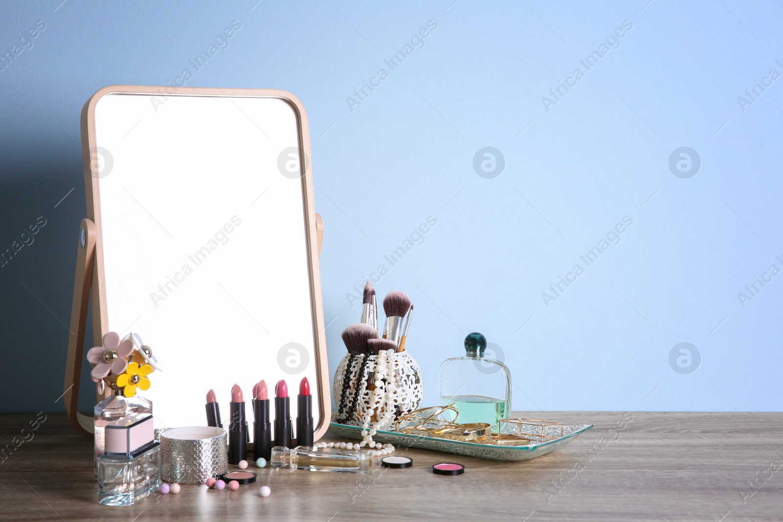 Photo of Stylish mirror, makeup products and accessories on table near light wall