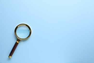 Photo of Magnifying glass on light blue background, top view. Space for text