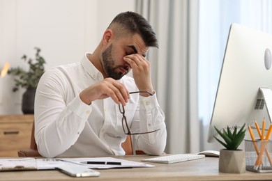 Overwhelmed man with glasses sitting at table in office