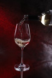 Photo of Pouring white wine from bottle into glass on color background